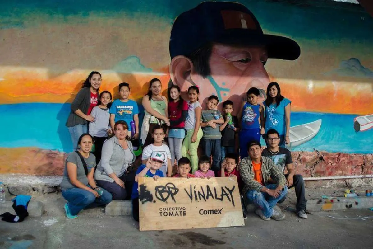 Niñas, niños y familias frente a un mural comunitario
